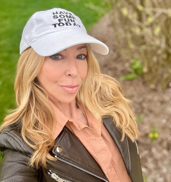 A woman wearing a white baseball cap with a text on it, posing outdoors.