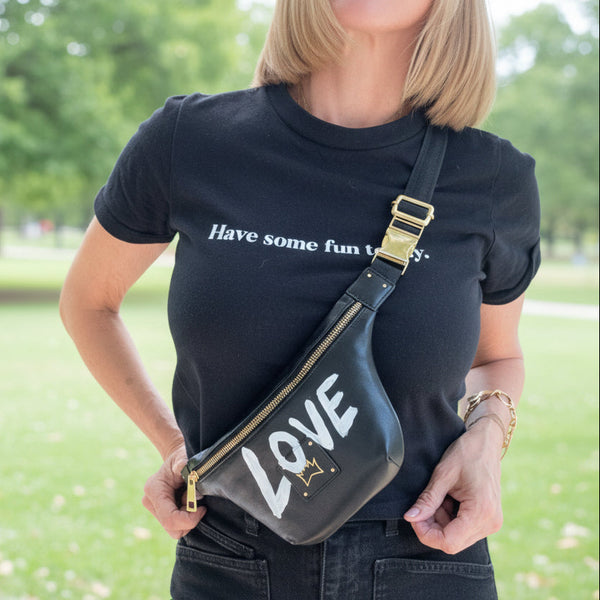 Person wearing a black t-shirt with text and holding a black fanny pack with 'LOVE' written on it.