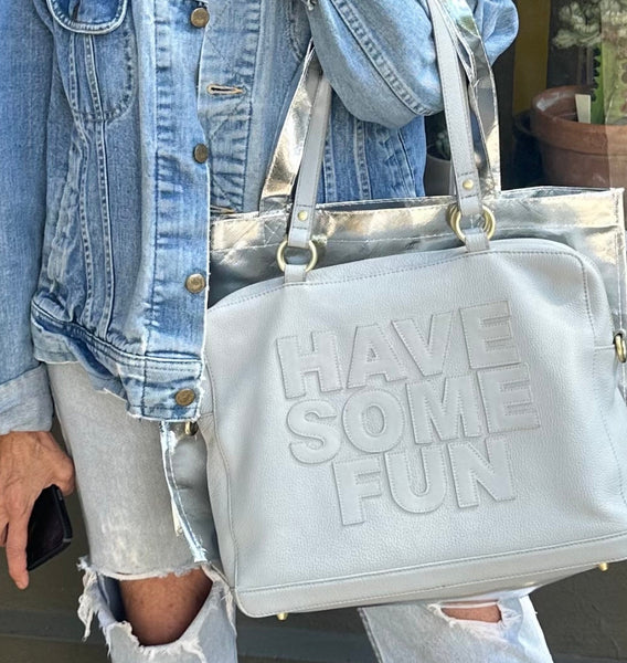 A person holding a grey pebbled leather handbag with gold hardware and the text 'HAZE SOME FUN' embossed on the front.