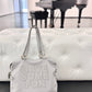 A light gray faux-leather handbag with the words 'HAVE SOME FUN' embossed on the front, resting on a white tufted bench in front of a blurred piano in a gallery space.