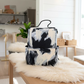 A black and white abstractly painted backpack with a top handle, displayed on a fluffy cream faux fur rug in a home interior setting.